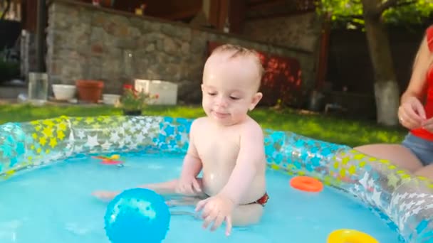 Портрет веселого мальчика, играющего с игрушками в бассейне в саду — стоковое видео