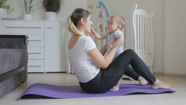 Beautfiul jovem mulher se exercitando no tapete de fitness segurando seu filho bebê bonito — Vídeo de Stock