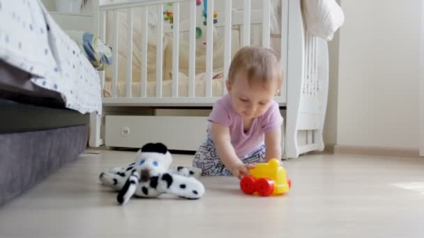 Dolly atış yerde yatarken ve oyuncak araba ile oynayan sevimli yürümeye başlayan çocuk — Stok video