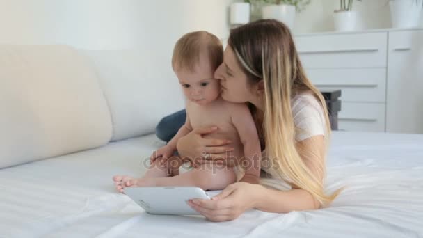 Красива молода мати лежить на ліжку зі своєю дитиною сом і використовує цифровий планшет — стокове відео