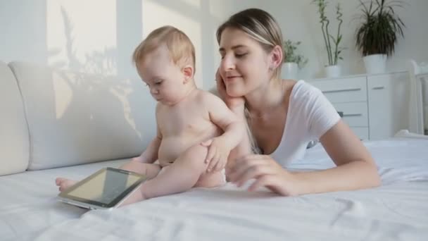 年轻美丽的母亲躺在床上和她的宝贝儿子和使用数字平板电脑 — 图库视频影像