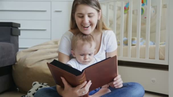 Boldog fiatal anya, baba fiú nagy könyvével a nappali padlón — Stock videók