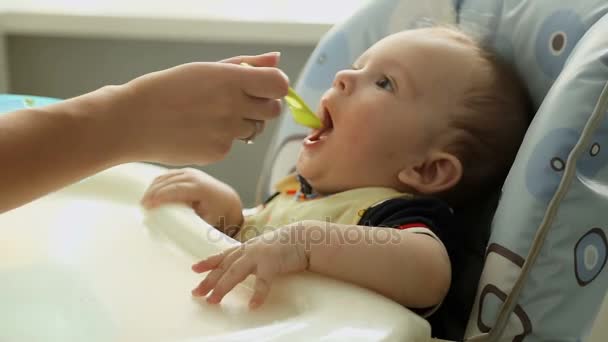 キッチンでベビーチェアにお粥を食べて空腹 1 歳男の子 — ストック動画