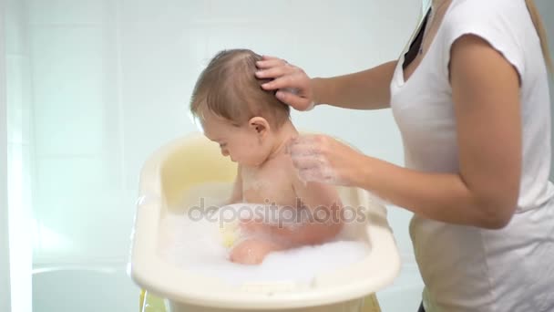 Imágenes en cámara lenta de la madre joven lavando al bebé en una bañera pequeña — Vídeo de stock