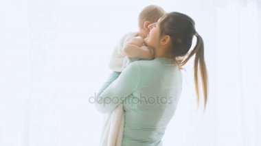 Ağır çekim görüntüleri bir holding ve bebeğini büyük pencerede sarılma anne