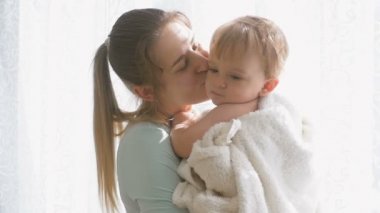 Mutlu genç anne sarılma ve öpüşme bebek oğlu büyük pencerede ağır çekim görüntüleri