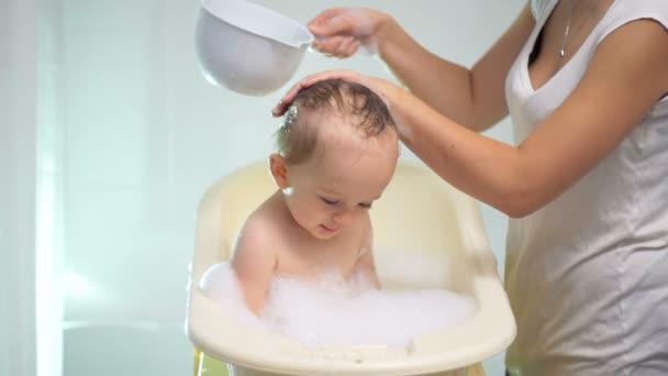 Slowmotion footage of mother pouring water over her baby at bathtub — Stock Video