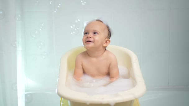 Imágenes en cámara lenta del lindo niño pequeño bañándose y mirando burbujas de jabón — Vídeos de Stock