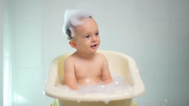 Mouvement lent de bébé garçon riant adorable appréciant prendre un bain avec des bulles de savon — Video