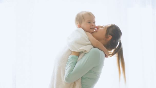 Imágenes en cámara lenta de la feliz madre sonriente criando a su hijo bebé en la ventana grande — Vídeos de Stock