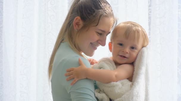 Imágenes en cámara lenta de la madre con un lindo bebé en toalla abrazándose a la ventana grande — Vídeos de Stock