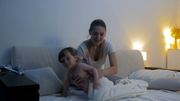 Beautiful young woman dressing her toddler son in bed at night — Stock Video