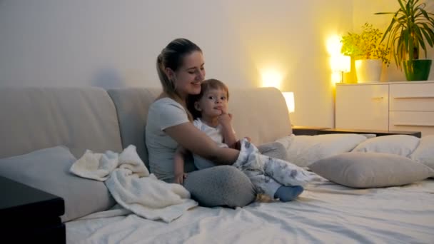 4 k film av ung mor klänningar hennes baby son i pyjamas innan du somnar — Stockvideo