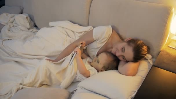 4k cuplikan lucu bayi laki-laki bermain di tablet sementara ibu tidur di sampingnya — Stok Video