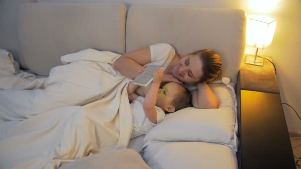 4k video de la madre joven acostada en la cama con su hijo pequeño y el uso de la tableta digital — Vídeos de Stock