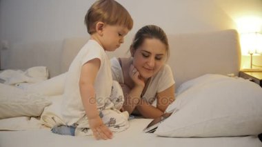 4 k görüntüleri bir yatakta yatan ve tablet çizgi film izlerken bebek ile anne