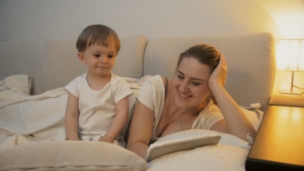 Mère avec bébé assis au lit et regardant des dessins animés sur tablette 