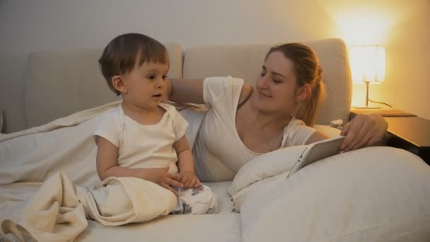 4k video of young mother using digital tablet with toddler son at night — Stock Video