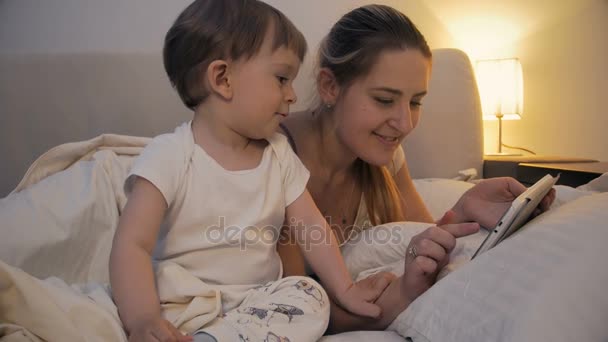 Images 4k de la mère avec bébé à l'aide d'une tablette sur le lit la nuit — Video