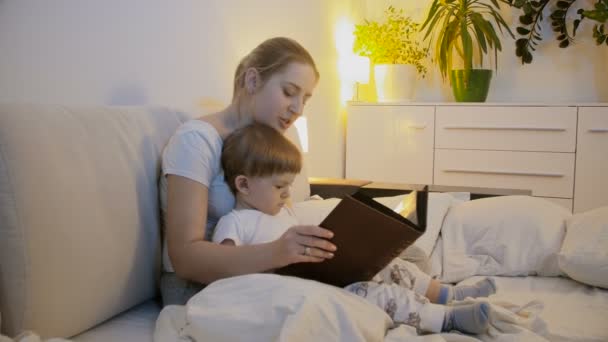 Cute toddler boy with young mother reading bedtime story in bed — Stock Video