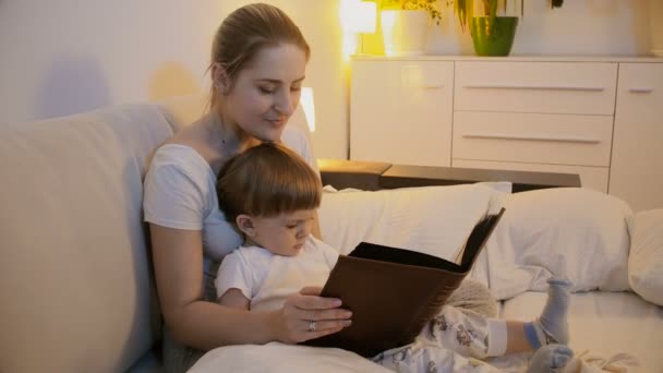 Happy leende mor och barn titta på fotografier i familjealbumet i sängen — Stockvideo