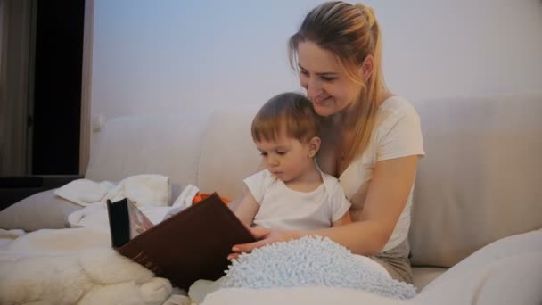 Cute toddler boy watching old family photographs in album with mother — Stock Video