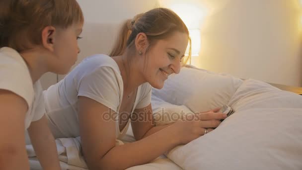 4k видео молодой матери, смотрящей кино на цифровой планшет в постели — стоковое видео