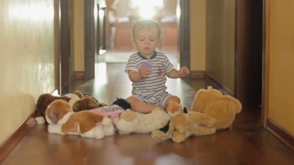 Adorable niño sonriente jugando con juguetes de peluche en el suelo de madera — Vídeos de Stock