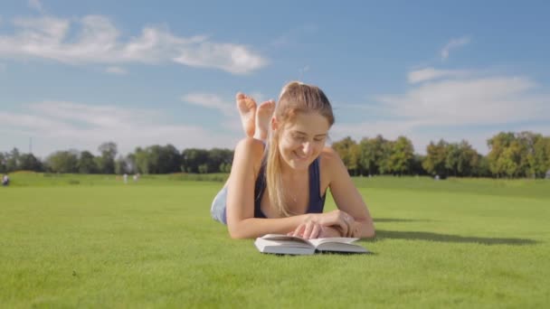 Portret van mooi lachende meisje het lezen van boek op het gras in park op warme zonnige dag — Stockvideo