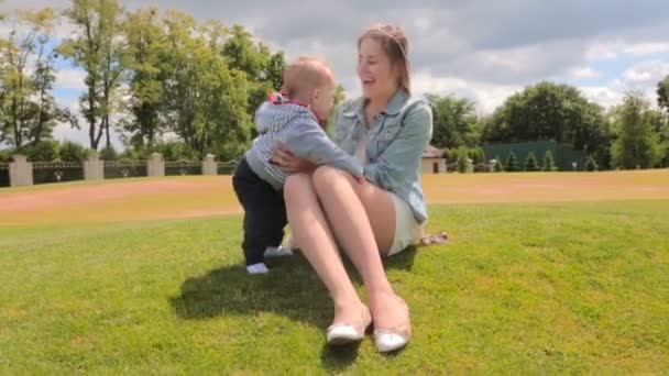 Allegro giovane donna che gioca con il suo figlio di 1 anno su erba al parco nella giornata di sole — Video Stock