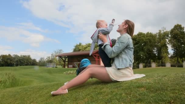 Feliz madre joven abrazándose y jugando con su pequeño hijo en la hierba en el parque — Vídeo de stock