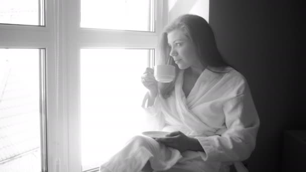 4k en blanco y negro video de hermosa mujer bebiendo café en el alféizar de la ventana — Vídeos de Stock