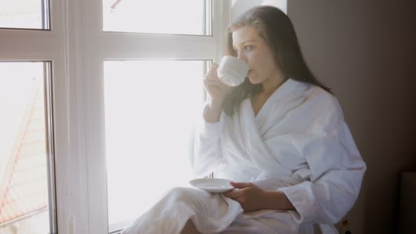 4 k beelden van jonge vrouw zittend op een vensterbank en koffie drinken — Stockvideo