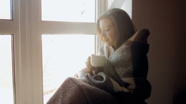 Genç kadının 4 k tonlu görüntüleri pencere kenarında oturan ve çay içme battaniyeye örtülü