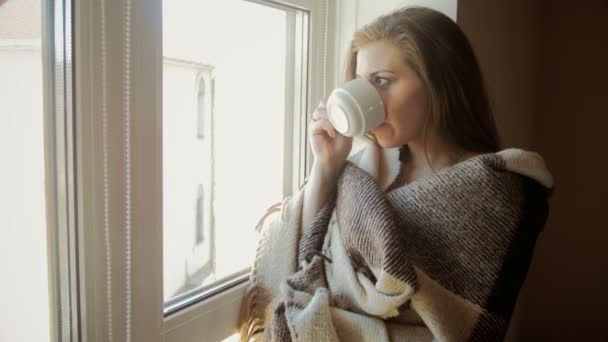 Primer plano tonificado video de mujer joven cubierta de cuadros bebiendo café en la ventana grande — Vídeos de Stock