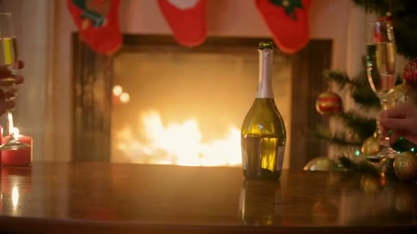 Las manos de la pareja en el amor tintineo vasos con champán en la víspera de Navidad. Hombre y mujer sentados en la chimenea en la sala de estar decorada . — Vídeos de Stock