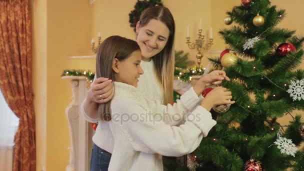 Porträt einer jungen lächelnden Mutter mit Tochter beim Schmücken des Weihnachtsbaums im Wohnzimmer — Stockvideo