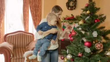 Erkek bebek üzerinde elele ve onun Noel ağacı gösteren mutlu genç anne. Hayattaki ilk Noel kavramı