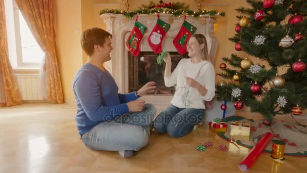 Gelukkige jonge paar zittend op de vloer in de woonkamer en plezier terwijl kerstboom versieren — Stockvideo