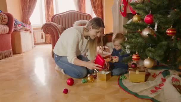 Junge schöne Mutter und 1-jähriger kleiner Sohn spielen unter dem Weihnachtsbaum im Wohnzimmer — Stockvideo