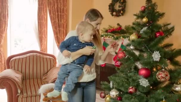 Šťastná mladá matka drží chlapeček na rukou a ukazuje mu vánoční stromeček. Koncept první Vánoce v životě