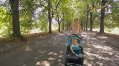 Steadicam atış mutlu gülümseyen anne bebek çocuk arabası ile sokak Park'ta yürüyüş