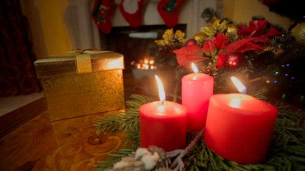 Nahaufnahme von drei brennenden Kerzen und goldener Weihnachtsgeschenkschachtel im Wohnzimmer