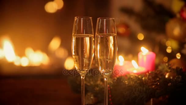 Gros plan de deux verres de champagne pétillant devant une cheminée en feu. Arbre de Noël décoré et bougies allumées sur fond . — Video