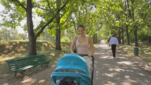 Gelukkig jonge vrouw die haar baby in kinderwagen in het park — Stockvideo