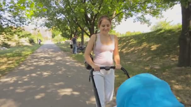 公園でベビーカーの赤ちゃんの息子と一緒に歩いている幸せな若い女性のステディカム ショット — ストック動画