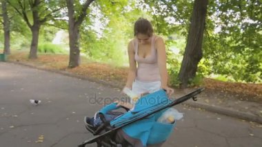 Genç anne çocuk arabası park oturan bebek oğlu şişe süt veren Steadicam atış