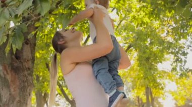 Genç anne parkta ağaçların altında yürümeye başlayan çocuk oğlu sarılma gülümseyen