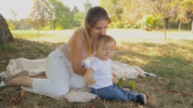 Mutlu genç anne bebek oğlu ile Park'ta üzerinde ağaç gölge battaniyeye oturmuş