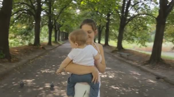 Steadicam sköt runt vackra leende kvinna kramar hennes baby son på park — Stockvideo